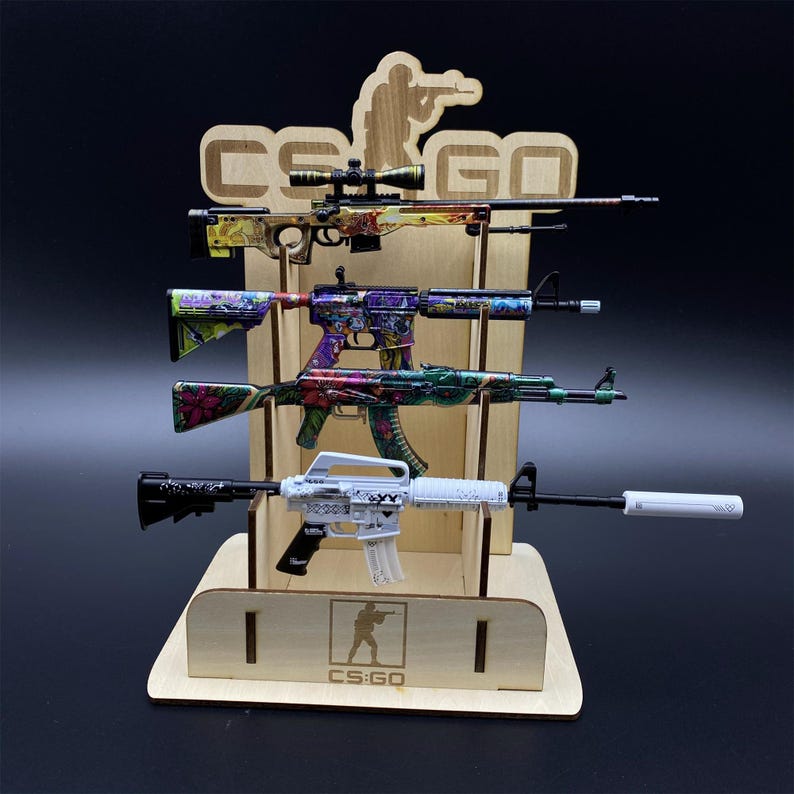 Puede incluir: Un expositor de madera con cuatro armas de juguete con dise&ntilde;os coloridos. El expositor tiene el texto "CS:GO" y una silueta de una persona sosteniendo un arma. Las armas de juguete presentan diversos patrones y colores.