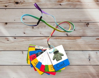 May include: A set of colorful flashcards with images and words for learning about clothing. The cards are attached to a rainbow lanyard. The cards include words like "Coat", "Boots", "Jumper", "Shirt", and "Hat".