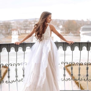 May include: A woman in a white wedding dress with a tulle skirt and a lace bodice stands on a balcony overlooking a city.