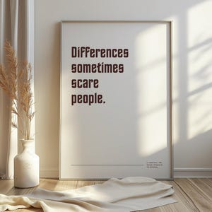Könnte beinhalten: Ein gerahmter Druck mit dem Text "Differences sometimes scare people" in einer fetten, dunkelbraunen Schrift. Der Druck wird vor einer weißen Wand präsentiert, mit einer Vase mit getrockneten Pflanzen und einem drapierten Stoff im Vordergrund.