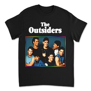 May include: Black t-shirt featuring the text "The Outsiders" in white above a colorful framed image of the cast. The image shows a group of men in various outfits. A classic movie-themed apparel item.