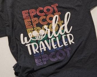 May include: A dark gray t-shirt with a rainbow-colored graphic that says "EPCOT world traveler EPCOT". The graphic features a stylized Mickey Mouse head with a globe inside.