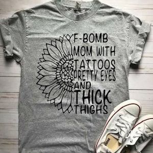 May include: Gray t-shirt with a black sunflower graphic and the text "F-Bomb Mom with Tattoos Pretty Eyes and Thick Thighs".