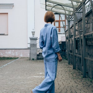 May include: A person wearing a light blue linen jumpsuit walks on a brick pathway. The person is facing away from the camera and has short brown hair.