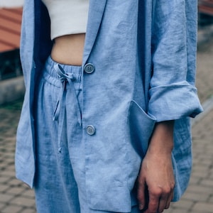 May include: A light blue linen blazer and matching pants. The blazer has a classic cut with a notched lapel and two button closures. The pants have a drawstring waist and a relaxed fit.