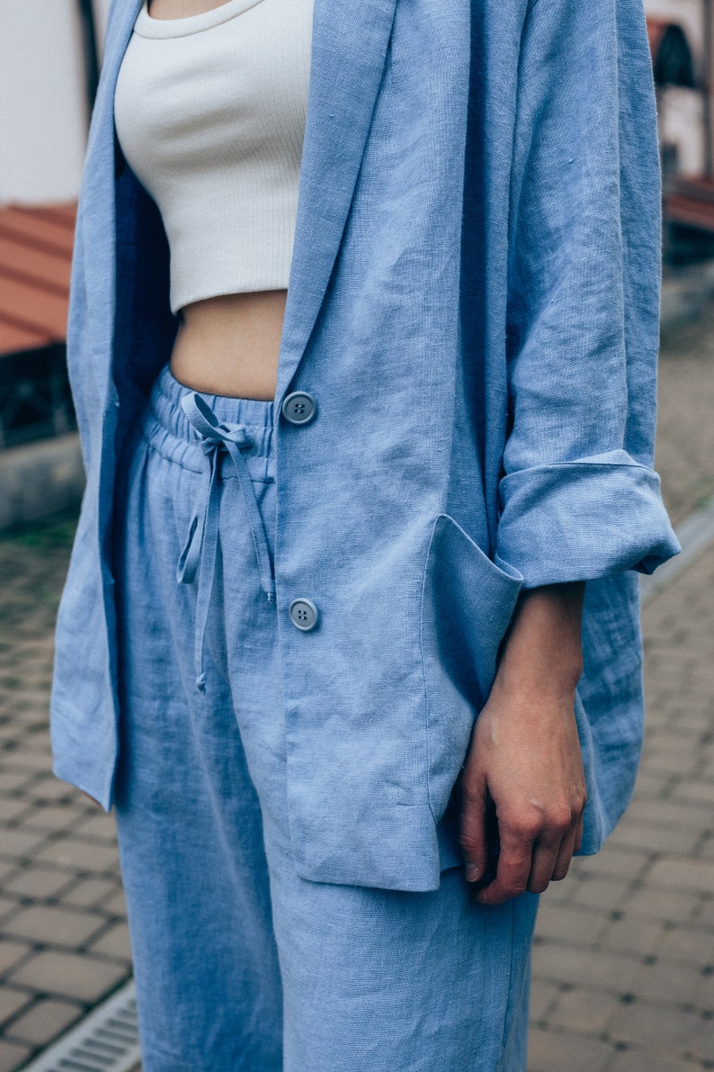 May include: A light blue linen blazer and matching pants. The blazer has a classic cut with a notched lapel and two button closures. The pants have a drawstring waist and a relaxed fit.