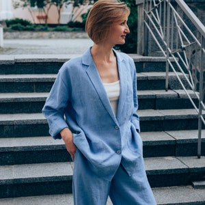 May include: A woman wearing a light blue linen suit jacket and matching pants. The jacket has a single button closure and the pants have a wide leg.
