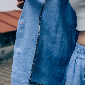 May include: A light blue linen blazer with a patterned lining. The blazer is unbuttoned and the lining is visible.