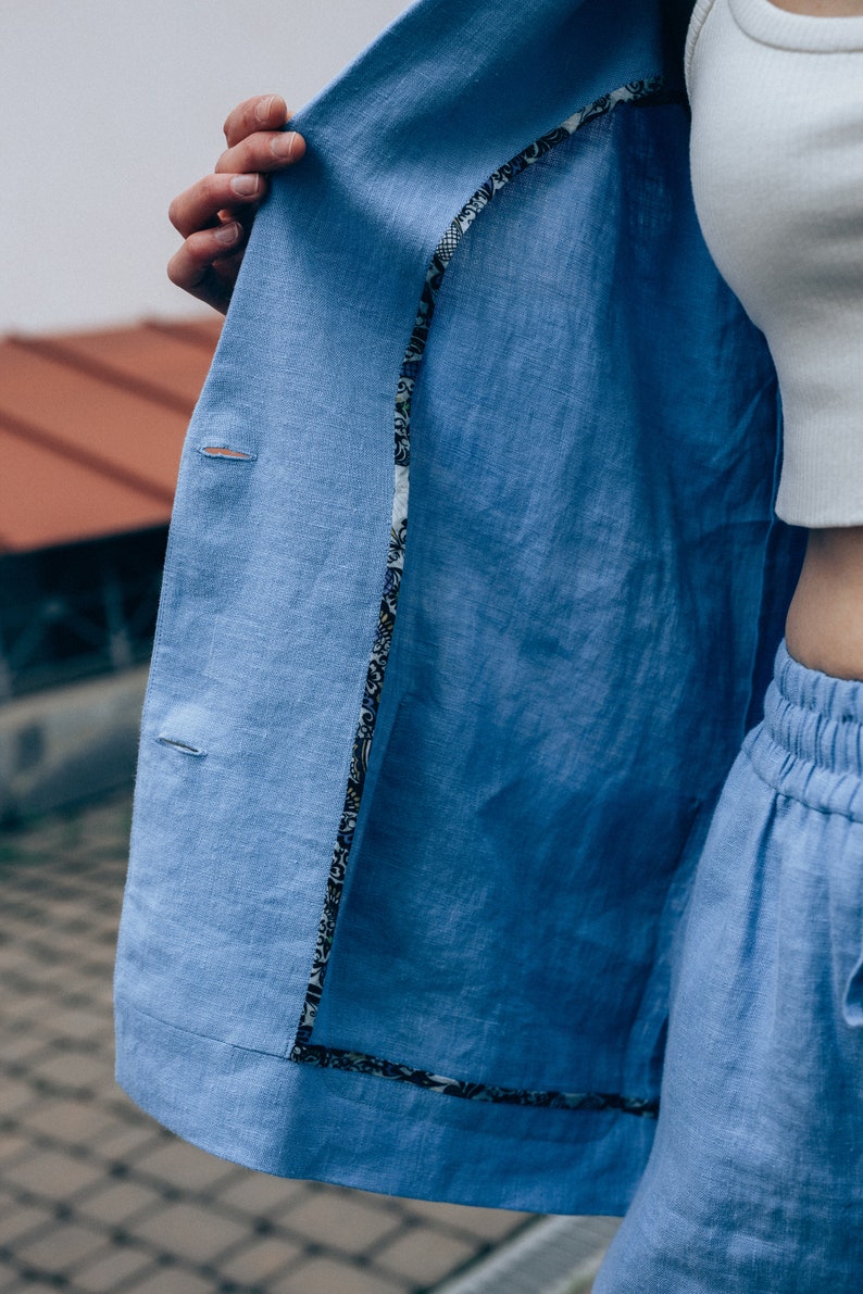 May include: A light blue linen blazer with a patterned lining. The blazer is unbuttoned and the lining is visible.
