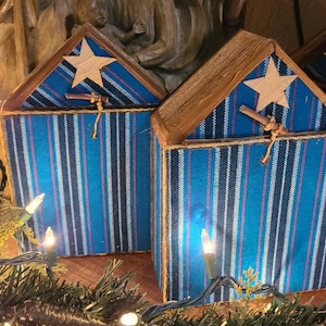Puede incluir: Tres cajas de madera rayadas en azul y blanco con una estrella en la parte delantera. Las cajas están decoradas con un palo marrón y una cuerda. Las cajas están sobre una superficie de madera.