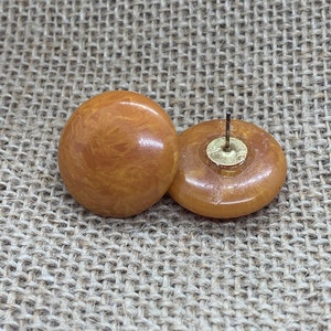 May include: A pair of amber-colored, round, resin earrings with a swirl pattern. The earrings have a post back.
