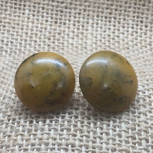 May include: A pair of round, yellow and black marbled earrings. The earrings are made of a smooth, glossy material.