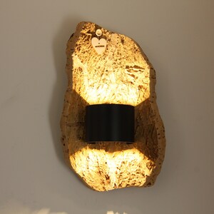 Puede incluir: Una taza de cerámica blanca con asa negra y el texto "But First, Coffee" en negrita negra. La taza se encuentra sobre un fondo borroso, sugiriendo un ambiente acogedor.