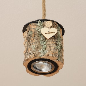May include: A pendant light fixture made from a natural cork log with a black metal base and a small heart-shaped tag that says "verkorkst".