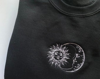 Puede incluir: Sudadera negra con un diseño bordado blanco de un sol y una luna.