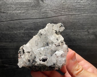 May include: A cluster of clear quartz crystals with a black matrix. The crystals are clustered together in a rough, natural formation.