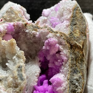 May include: A geode with a cavity filled with vibrant purple crystals. The outer rock is a mix of grey, brown, and white, with a rough texture. The crystals inside are a deep, saturated purple, creating a striking contrast.