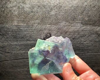 May include: A cluster of green and purple fluorite crystals with a natural, rough texture.