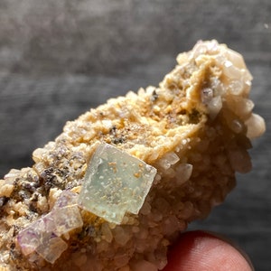 以下が含まれることがあります： 白い水晶の母岩に埋め込まれた、薄い緑色と紫色の蛍石の結晶の塊