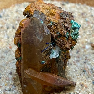 May include: A cluster of brown, green, and clear crystals with a rough, textured surface. The crystals are arranged in a random pattern and appear to be naturally formed.