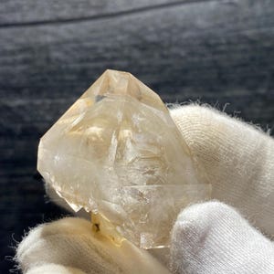 May include: A clear, faceted quartz crystal with a light brown hue. The crystal is shaped like a pyramid with a pointed top and a flat base.