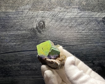 May include: A green, purple and white fluorite crystal cluster on a matrix of rock. The crystal is a cubic shape and has a glossy finish.