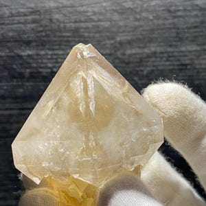 May include: A clear, faceted, golden quartz crystal with a pointed top and a base that is a cluster of smaller crystals.