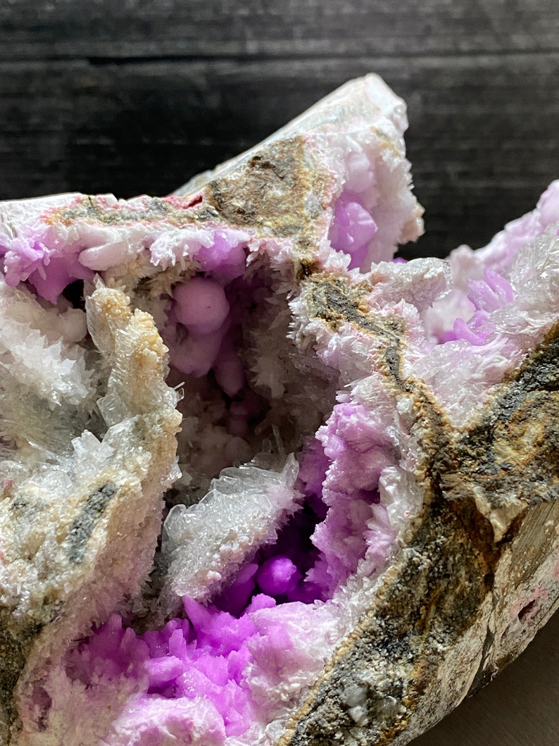 May include: A close-up of a mineral specimen with a cavity filled with vivid purple crystals. The outer matrix is a mix of white, grey, and brown, creating a striking contrast. The crystals have a sparkling, textured appearance, showcasing natural formations.