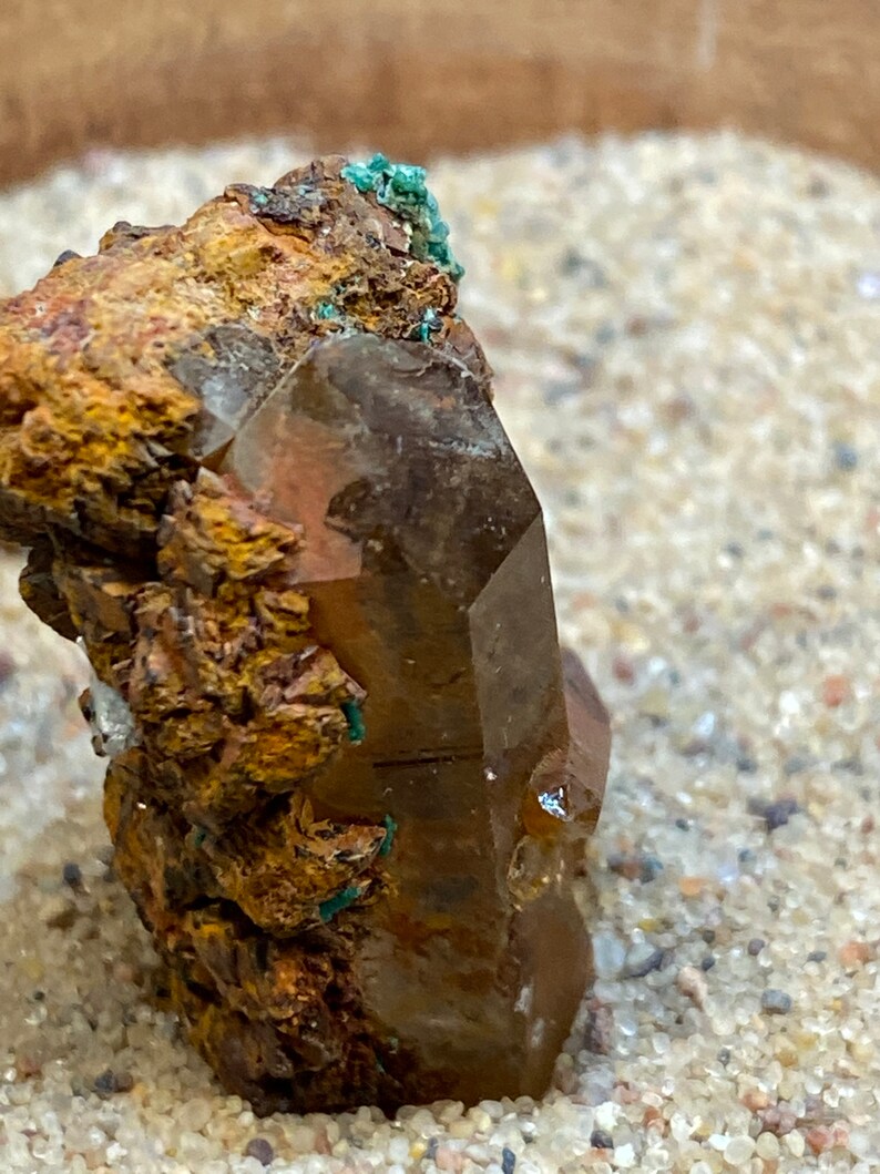 May include: A large, clear quartz crystal with a brown, rusty coating. The crystal is surrounded by smaller, brown, rusty crystals.