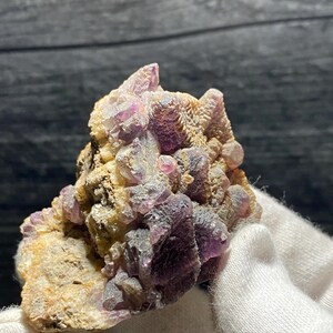 May include: A cluster of purple fluorite crystals with a rough, natural texture. The crystals are clustered together in a small, irregular shape.