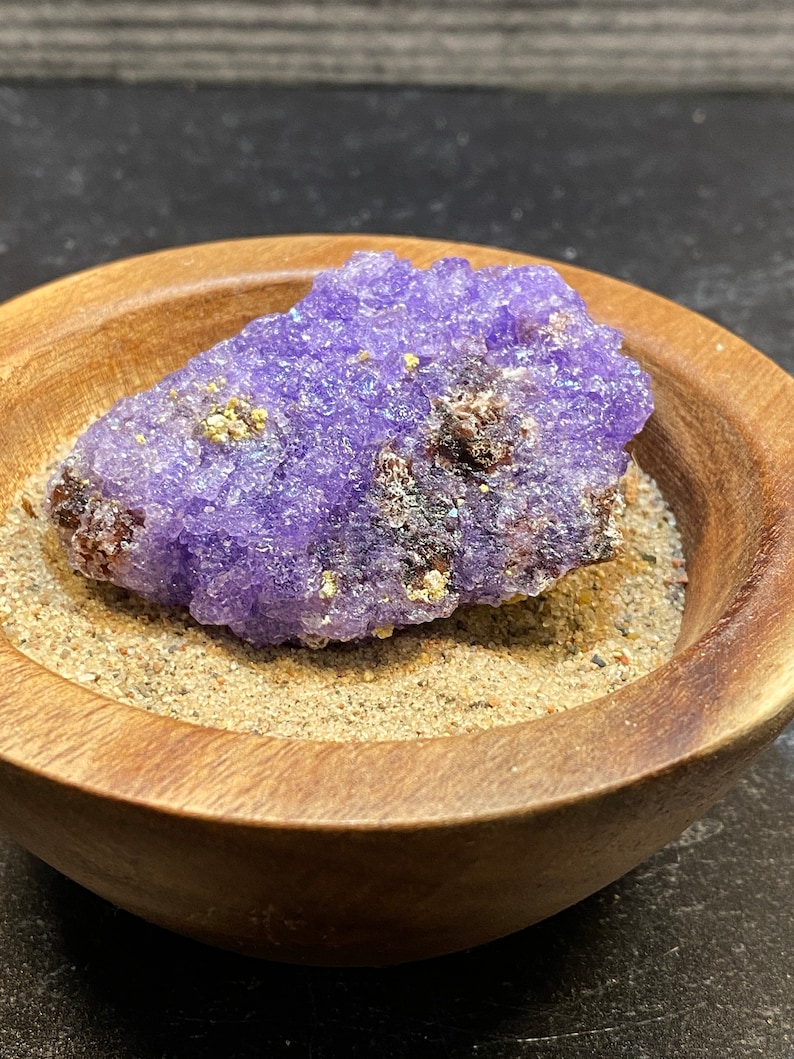 Puede incluir: Un c&uacute;mulo de cristales p&uacute;rpura y dorado en un cuenco de madera. El cristal es un c&uacute;mulo de peque&ntilde;os cristales brillantes.