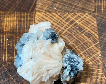 May include: A cluster of white barite crystals with a few black crystals. The crystals are arranged in a cluster and have a rough, natural texture.