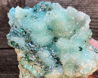 May include: A cluster of light blue and white crystals with a green and brown base. The crystals are clustered together in a rough, natural formation.