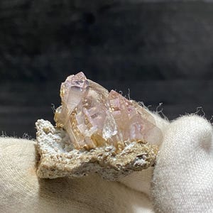 以下が含まれることがあります： ピンクがかった色合いの小さな透明な水晶の塊が、ざらざらした茶色のマトリックスに埋め込まれています。水晶は半透明で、わずかに輝いています。
