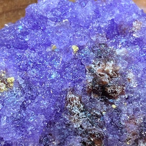 Puede incluir: Primer plano de un c&uacute;mulo de cristal de amatista p&uacute;rpura con una superficie rugosa y texturizada. El cristal tiene un color p&uacute;rpura intenso con un ligero brillo iridiscente.