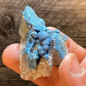 May include: A cluster of blue azurite crystals on a clear quartz matrix. The azurite crystals are clustered together in a rounded shape, and the quartz matrix is translucent.