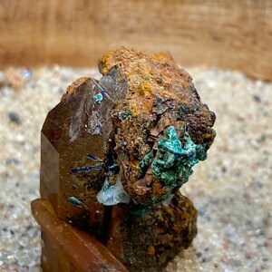 May include: A cluster of brown, clear, and green crystals with a rough, textured surface. The crystals are arranged in a vertical stack and appear to be naturally formed.