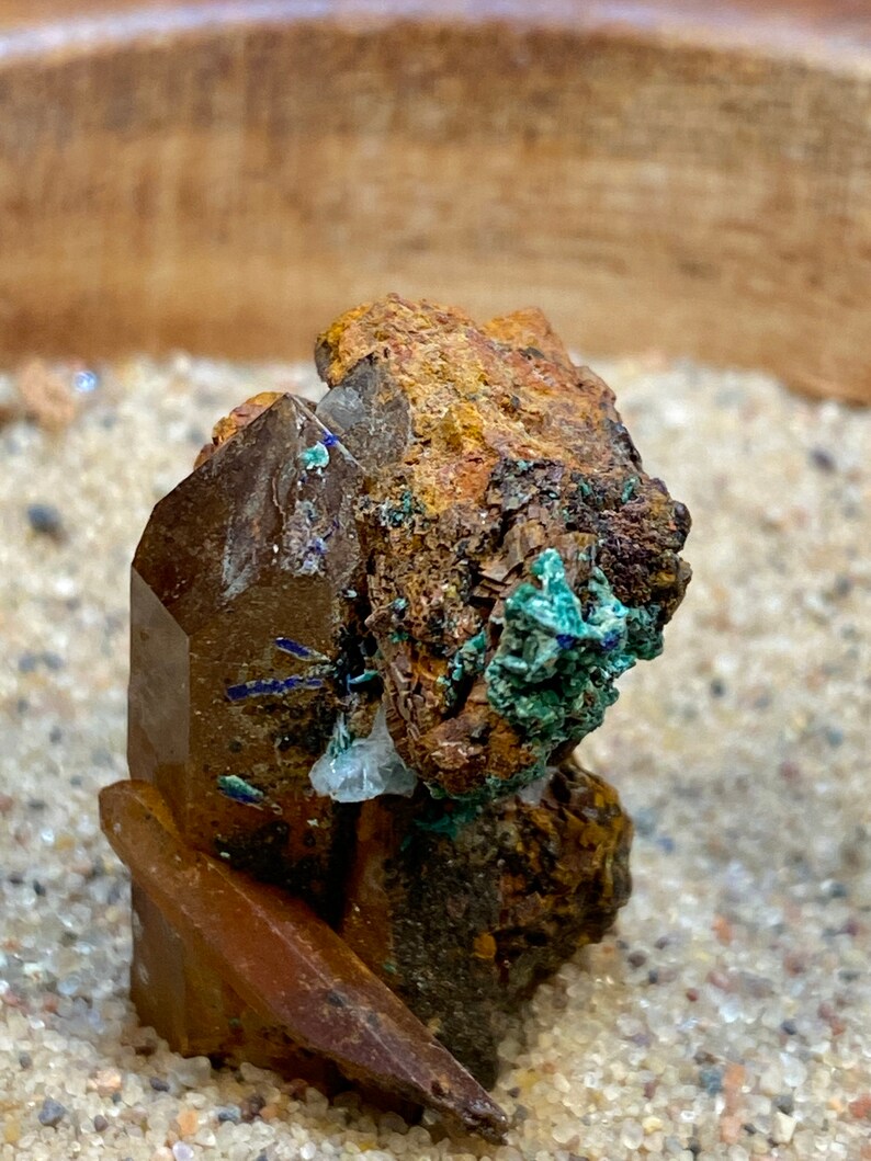May include: A cluster of brown, clear, and green crystals with a rough, textured surface. The crystals are arranged in a vertical stack and appear to be naturally formed.