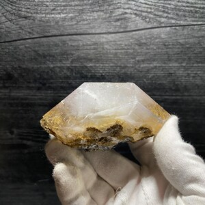 May include: A clear, white, faceted crystal with a brown, rough, natural base. The crystal is shaped like a pyramid with a flat top.