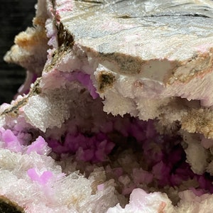 May include: Close-up of a geode featuring a cavity filled with vibrant purple crystals. The outer layer is a mix of grey, white, and pink hues, creating a striking contrast. The crystals are clustered, adding texture and visual interest.