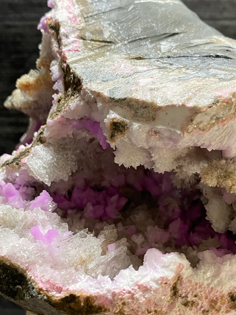 May include: Close-up of a geode featuring a cavity filled with vibrant purple crystals. The outer layer is a mix of grey, white, and pink hues, creating a striking contrast. The crystals are clustered, adding texture and visual interest.