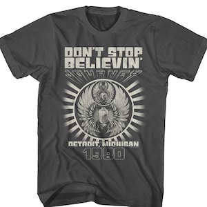 May include: A dark gray t-shirt with a white graphic design featuring the text "Don't Stop Believin'" and "Journey" with a winged scarab beetle design. The text "Detroit, Michigan 1980" is also included in the design.