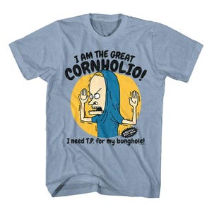 May include: Light blue t-shirt featuring a cartoon character in a blue robe with the text "I AM THE GREAT CORNHOLIO!" and "I need T.P. for my bunghole!". The graphic is set against a yellow circle.