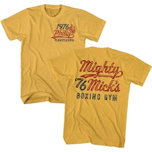 May include: Mustard yellow t-shirt with the text "1976 Philly Pennsylvania" on the front and "Mighty '76 Mick's Boxing Gym" on the back. The text is in red, blue, and black.