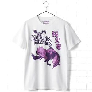 May include: A white short-sleeve t-shirt featuring a purple graphic print of a creature from Monster Hunter. The design includes the text Monster Hunter in a stylized font, Japanese characters, and the American Classics logo on the inner neck label.