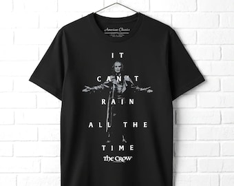 May include: A black short-sleeved t-shirt featuring a graphic of a figure with arms outstretched. The white text reads IT CAN'T RAIN ALL THE TIME and THE CROW. The shirt is displayed on a hanger, showcasing a crew neckline and a standard fit design.