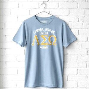 May include: A light blue short-sleeve t-shirt featuring the white text "American Classics" inside the collar. The chest displays the white text "LAMBDA EPSILON OMEGA" above large gold Greek letters and the white text "OLD SCHOOL" at the bottom.