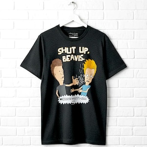 May include: A black short-sleeve t-shirt featuring a graphic of the cartoon characters Beavis and Butt-Head. The text above the characters reads SHUT UP, BEAVIS. Below the characters is a white jagged shape containing the text BEAVIS AND BUTT-HEAD.