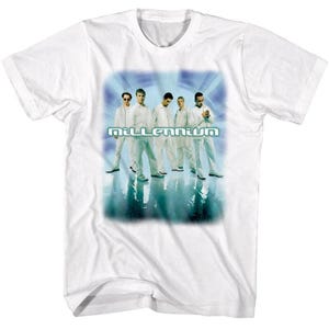 May include: White t-shirt featuring a group of five people in white outfits, standing in front of a blue and teal background. The word "Millennium" is printed in a light blue, stylized font across the center of the image.