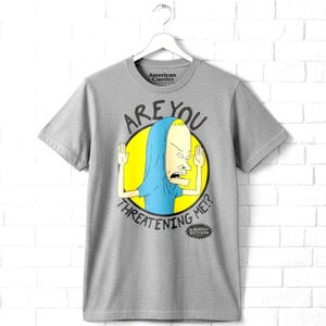 May include: A heather grey short-sleeve t-shirt featuring a graphic of the character Beavis from Beavis and Butt-Head. The character is inside a yellow circle with the text ARE YOU THREATENING ME? and the show logo at the bottom.